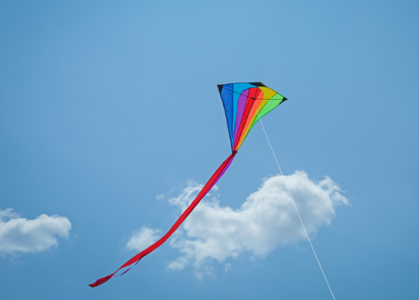 Ein bunter Drachen fliegt hoch in den blauen Himmel, nur zwei kleine Wolken