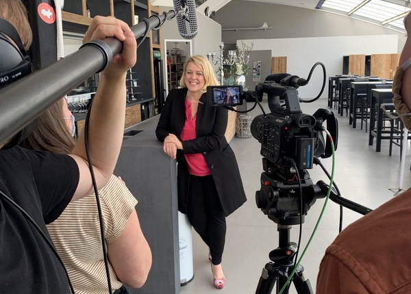 Am Set einer Filmproduktion, eine Frau wird interviewt, einer hält das Richtmikrofon, einer steht hinter der Kamera