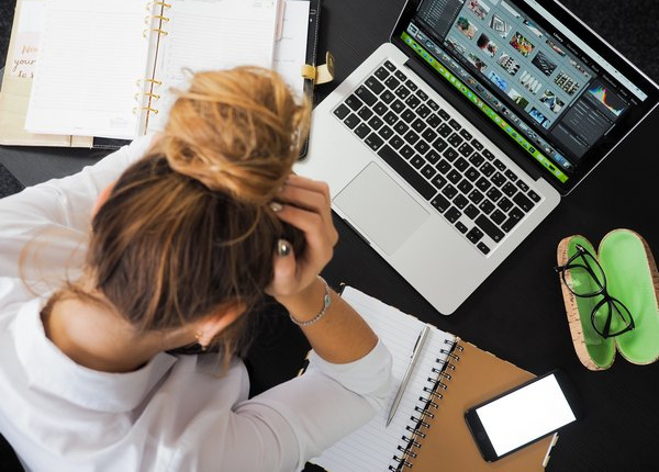 Blick von oben auf eine Frau, sie rauft sich - vor Laptop und Notizen sitzend - die Haare